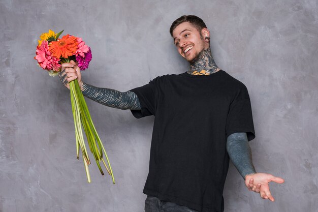 Happy young man holding gerbera flowers in hand shrugging against grey wall