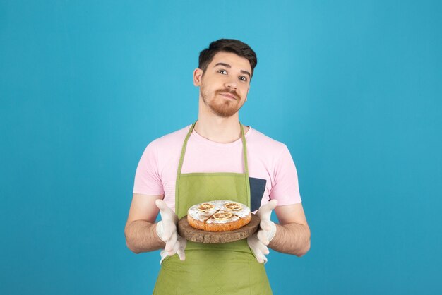 Happy young man holding homemade fresh cake and looking at camera.