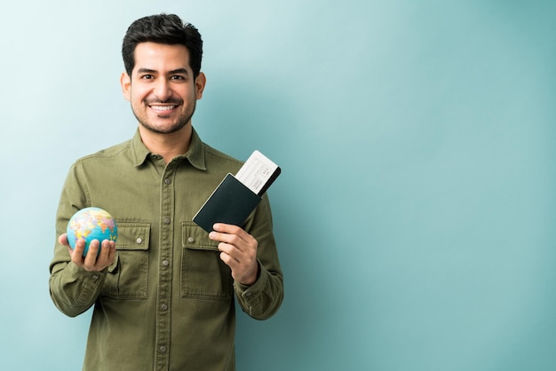 Бесплатное фото Счастливый молодой человек с паспортом и посадочным талоном с глобусом, стоя на синем фоне