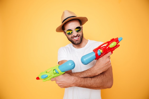 Бесплатное фото Счастливый молодой человек держит игрушечные водяные пистолеты