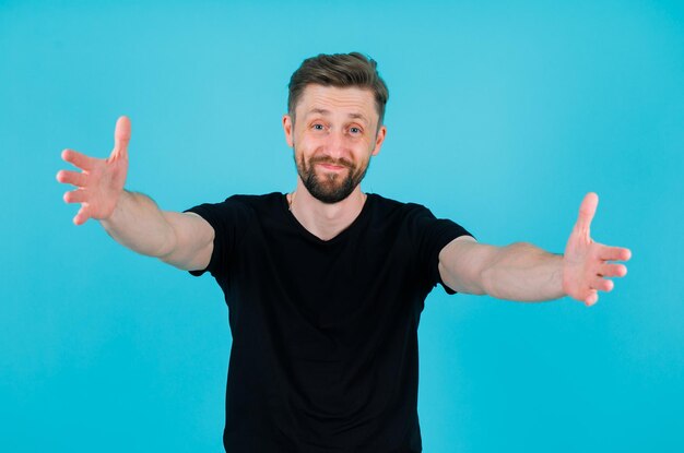 Happy young man is opening arms by extending them to camera on blue background