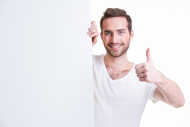 Счастливый молодой человек смотрит из пустого баннера с большим пальцем вверх - изолированные на белом