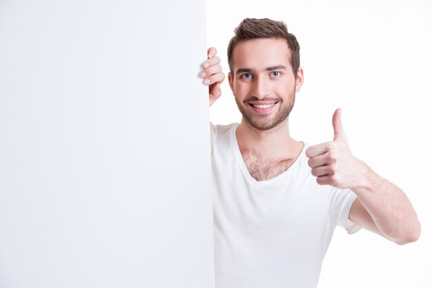 Happy young man look out from blank banner with thumb up - isolated on white