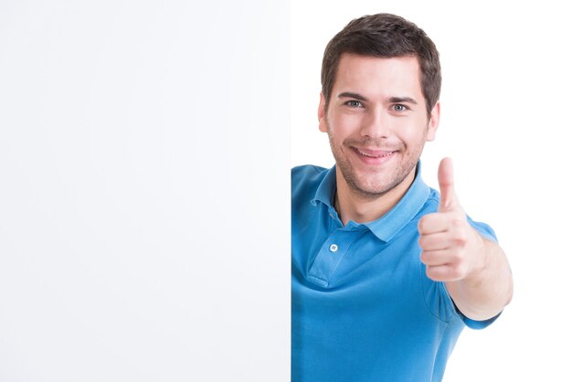 Happy young man look out from blank banner with thumb up - isolated on white.