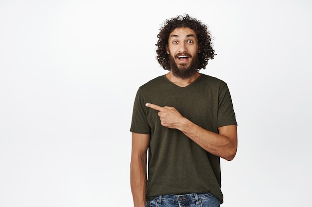 驚いた人差し指を探している幸せな若い男は、白い背景の上にTシャツに立っている広告を示しています