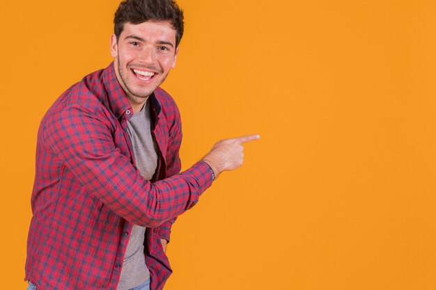 Happy young man pointing his finger on an orange background