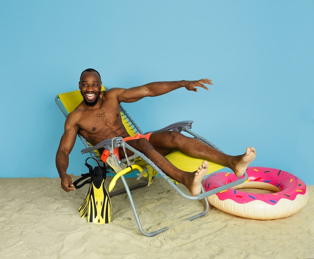 행복 한 젊은 남자 휴식 하 고 푸른 공간에 도넛으로 해변 반지와 함께 laughting