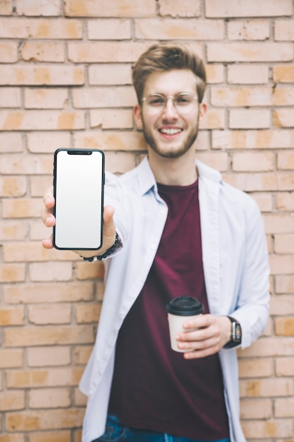 Foto gratuita giovane felice che mostra telefono cellulare con lo schermo bianco in bianco