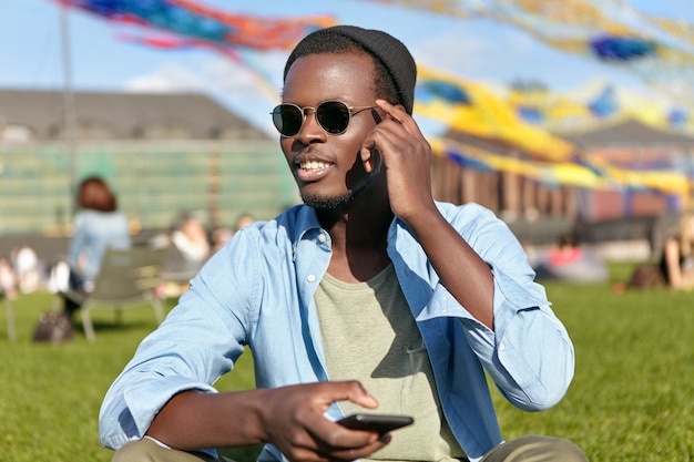 Happy young man sitting on the grass with his phone