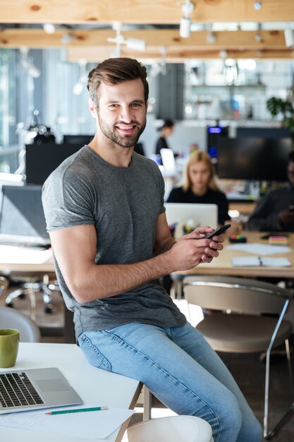 Счастливый молодой человек сидит на столе в офисе в чате