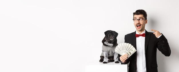 Free photo happy young man in suit earn money with his dog guy rejoicing holding dollars and pointing left blac