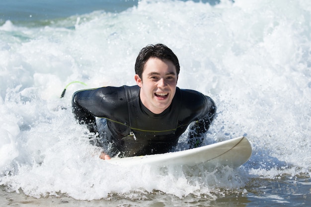 Happy young man swimming on surfboard in ocean