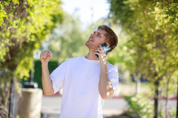 電話で話している幸せな若い男が公園で彼女の拳を絞る