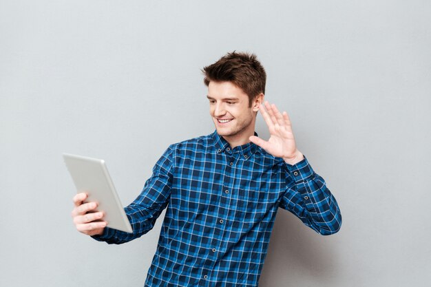 Happy young man waving to friends by tablet computer