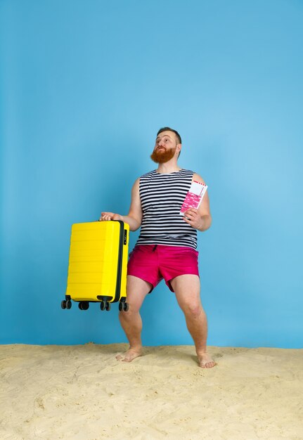 Happy young man with bag prepared for traveling on blue  space