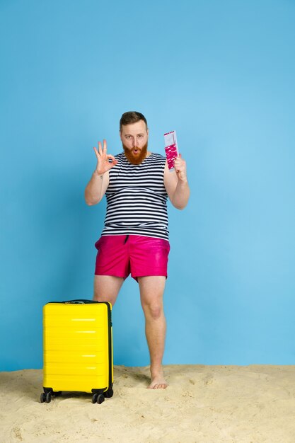 Happy young man with bag prepared for traveling on blue  space