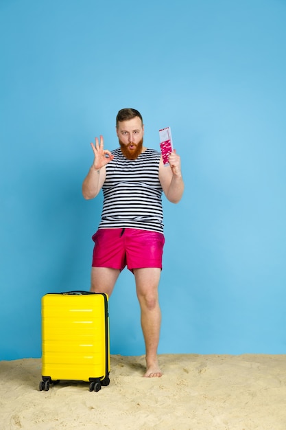 Happy young man with bag prepared for traveling on blue  space