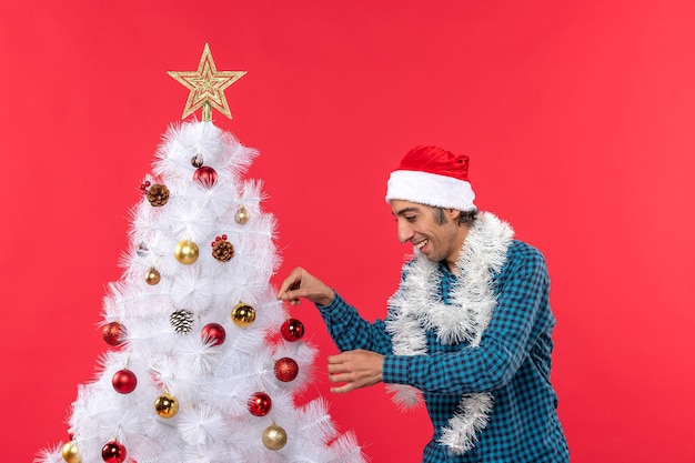 Happy young man with santa claus hat in a blue stripped shirt and decorating his xsmas tree on red