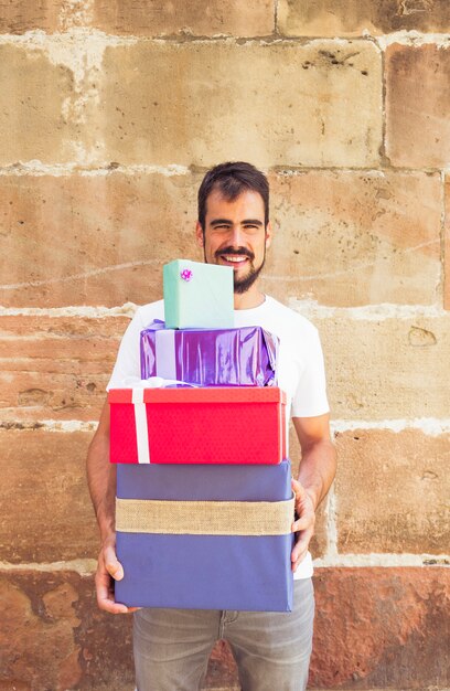 Happy young man with stacked gifts against grunge wall