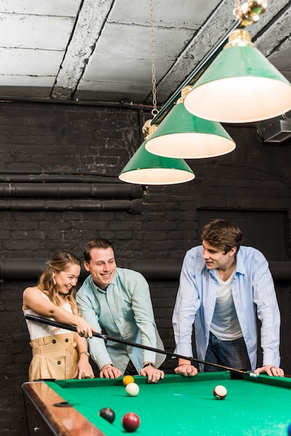 Happy young men and woman playing billiards at club