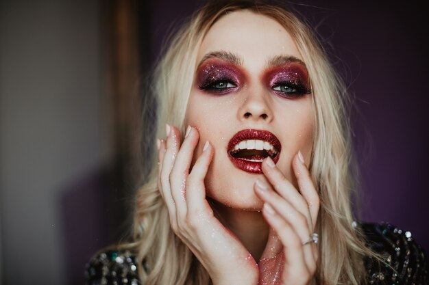 Happy young model with trendy makeup expressing good emotions. Indoor photo of graceful caucasian woman with blonde wavy hair.