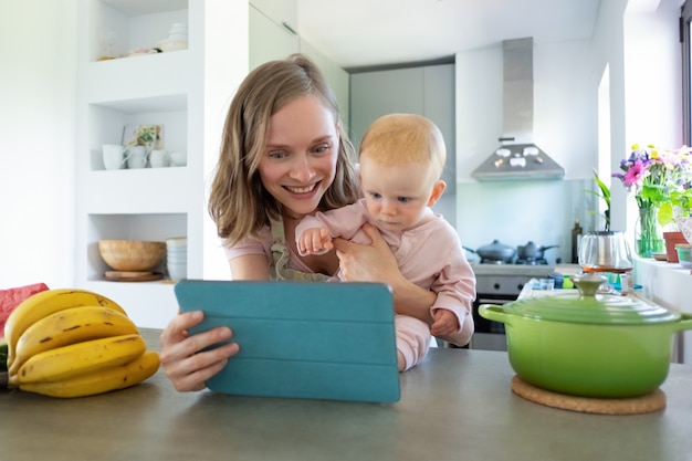 Felice giovane mamma e bambino guardando il corso di cucina video online su tablet mentre si cucina insieme in cucina. cura dei bambini o cucinare a casa concetto