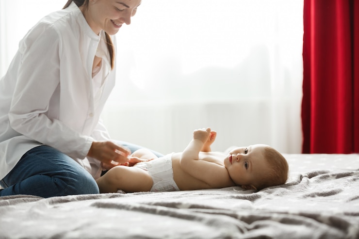 Free Photo happy young mom in light bedroom smiles and dressing her precious baby boy for a morning walk in park. family concept..