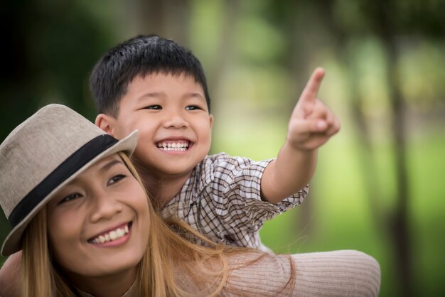 幸せな若い母親と息子は、彼女の背中にピギーバックを乗せている小さな男の子を笑っています。