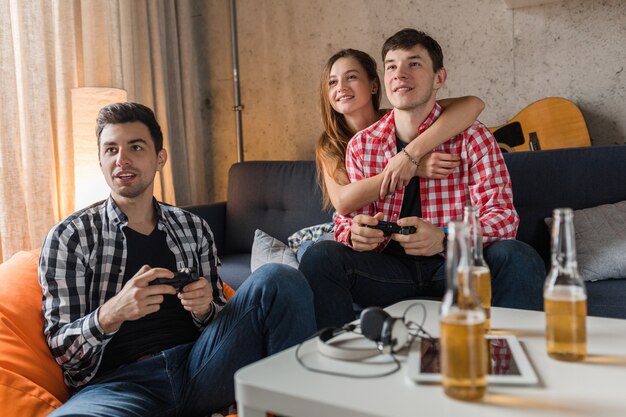 Happy young people playing video games, having fun, friends party at home, close up hands holding joystick, hipster company together, smiling, positive, laughing, competition, beer bottles on table