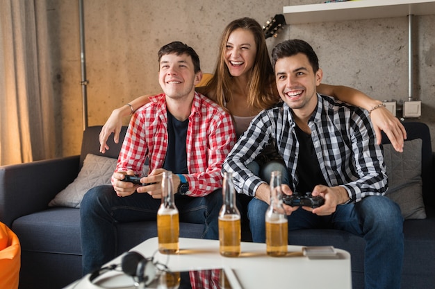 Счастливые молодые люди, играющие в видеоигры, веселящиеся, вечеринка с друзьями дома, хипстерская компания вместе, двое мужчин и одна женщина, улыбающиеся, позитивные, расслабленные, эмоциональные, смеющиеся, соревнования