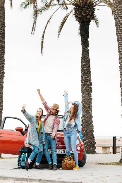 Happy young people taking selfie near red car in street 