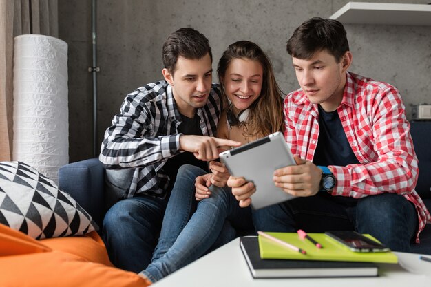 Happy young people using tablet, students learning, having fun, friends party at home, hipster company together, two men one woman, smiling, positive, online education