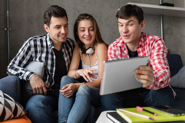 Happy young people using tablet, students learning, having fun, friends party at home, hipster company together, two men one woman, smiling, positive, online education