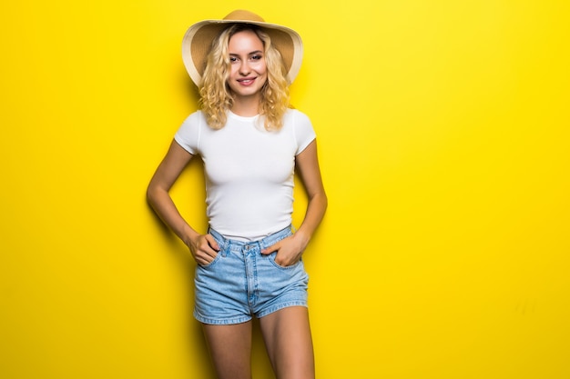 Free photo happy young pretty woman straw hat posing on yellow wall