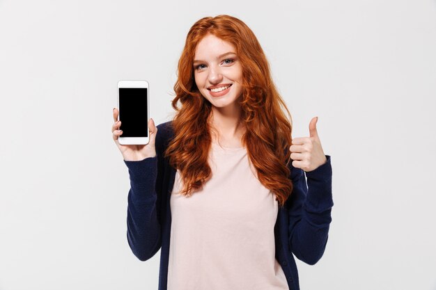 携帯電話の表示を示す幸せな若い赤毛の女性