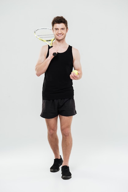 Happy young sportsman holding tennis ball and racket.