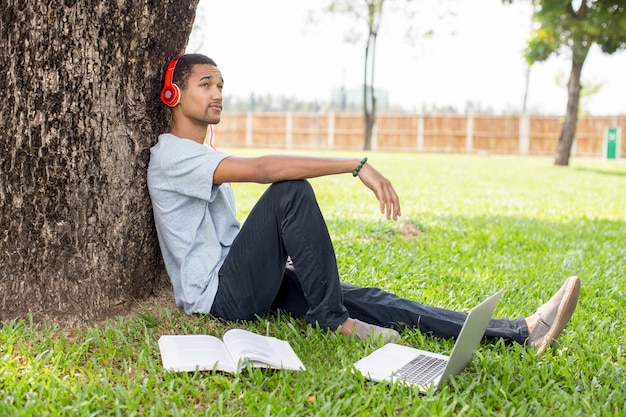 Happy young student man listening to music in park