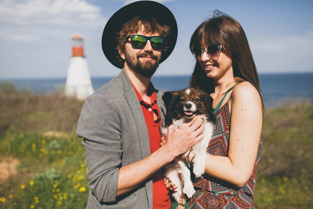 Happy young stylish hipster couple in love walking with dog in countryside