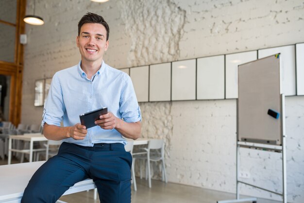 Happy young stylish smiling man in co-working office, startup freelancer holding using tablet,