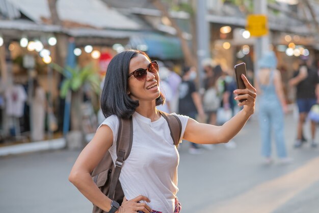 Женщина счастливого молодого перемещения азиатская используя мобильный телефон и ослабляет на улице.