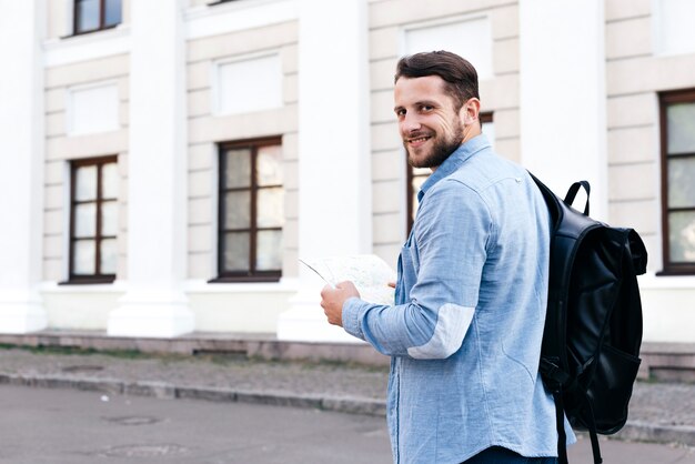 Happy young traveler man holding map and looking at camera