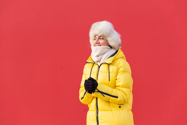 Felice giovane donna sullo sfondo di un muro rosso in vestiti caldi in una giornata di sole invernale