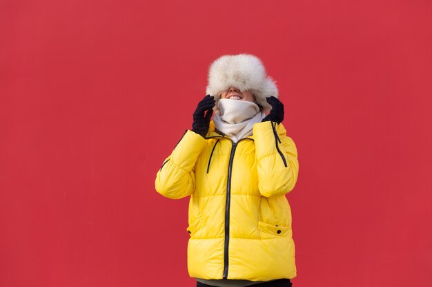 冬の晴れた日に暖かい服を着て赤い壁の背景に幸せな若い女性