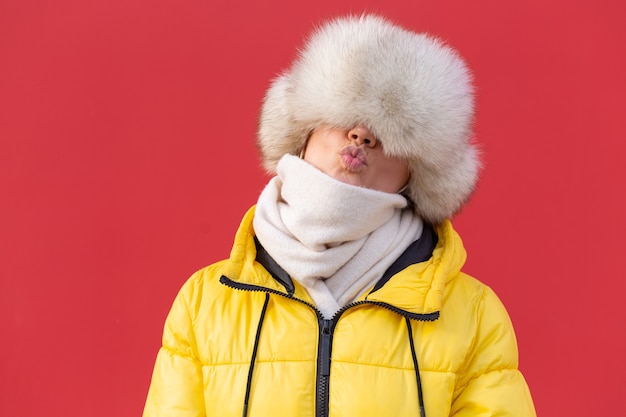 Happy young woman on the background of a red wall in warm clothes on a winter sunny day