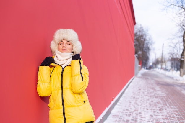 冬の晴れた日に暖かい服を着て赤い壁の背景に幸せな若い女性