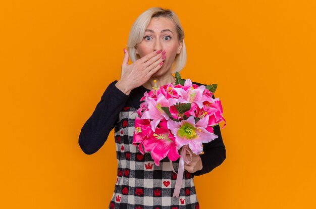 Happy young woman in beautiful dress holding bouquet of flowers looking at camera