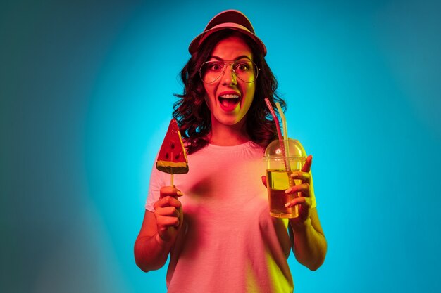 Happy young woman in a cap holding sweets and drink over trendy blue neon