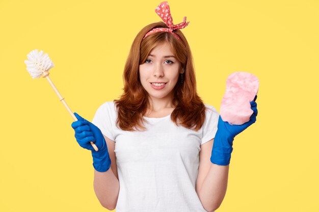 Счастливая молодая женщина в повседневной одежде, держит щетку и швабру, рекламирует чистящие средства