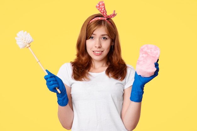 Happy young woman in casual clothes, holds brush and mop, advertises cleaning supplies