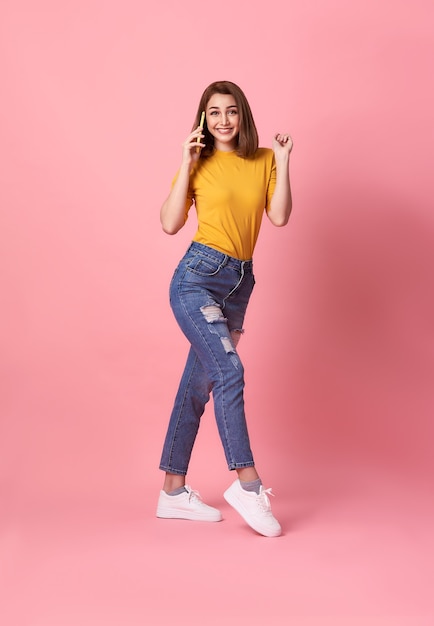 Happy young woman celebrating with mobile phone isolated over pink background.